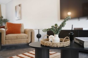 A modern living room with a round black table, a beige sofa, and a television mounted on the wall.