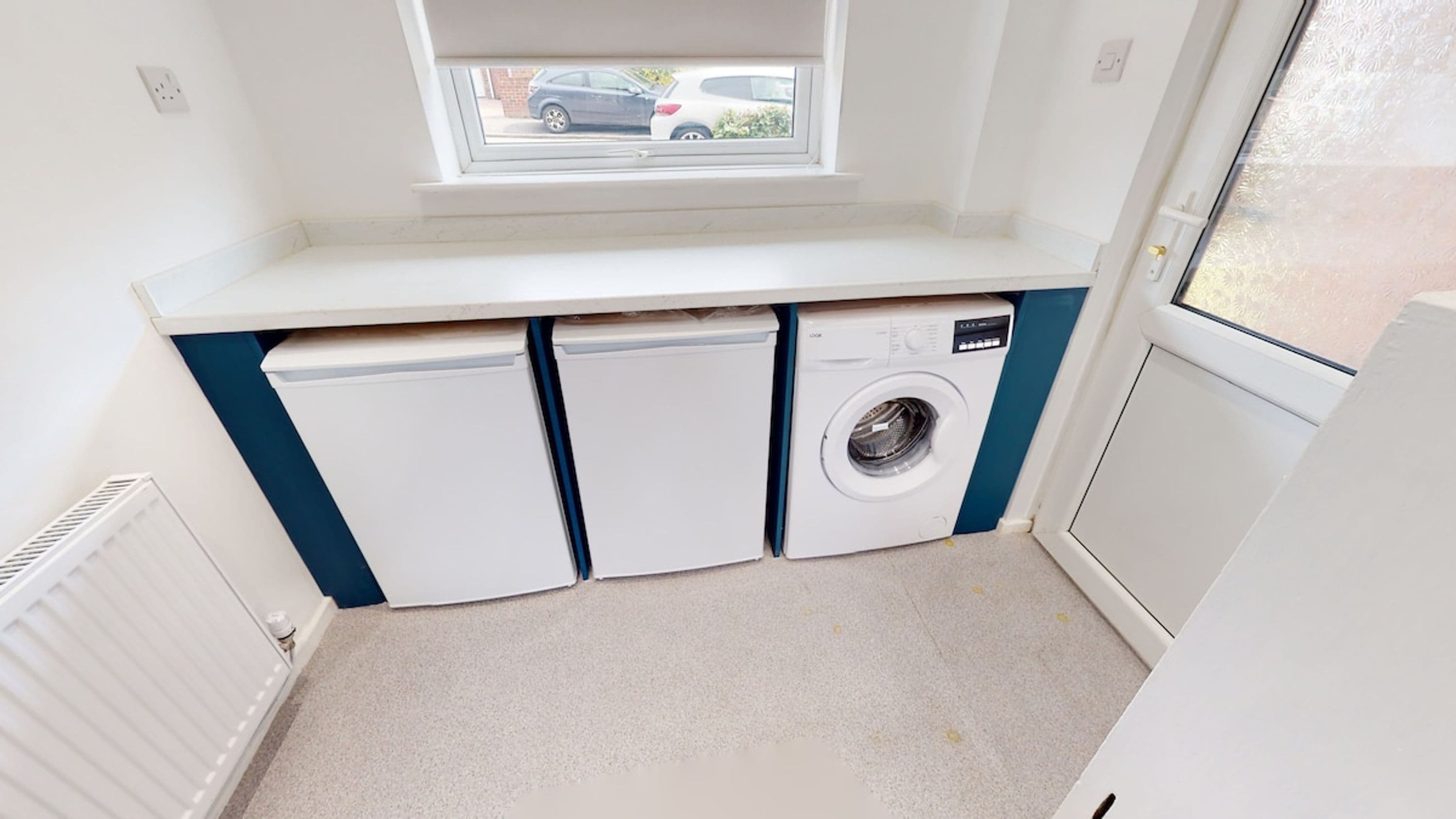 A compact laundry room with a washing machine, two dryers, and a window above the appliances.