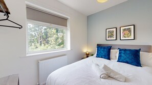 A bedroom with a large bed, a window with a view of trees, and two framed pictures on the wall. - Daventry House Horizon Stays (Stockton-on-Tees)