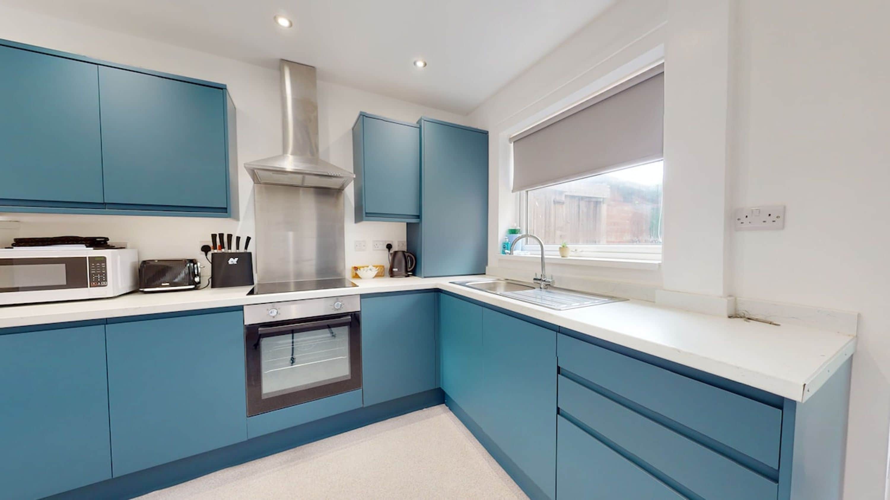A modern kitchen with blue cabinets, a stainless steel range hood, a microwave, and a built-in oven.