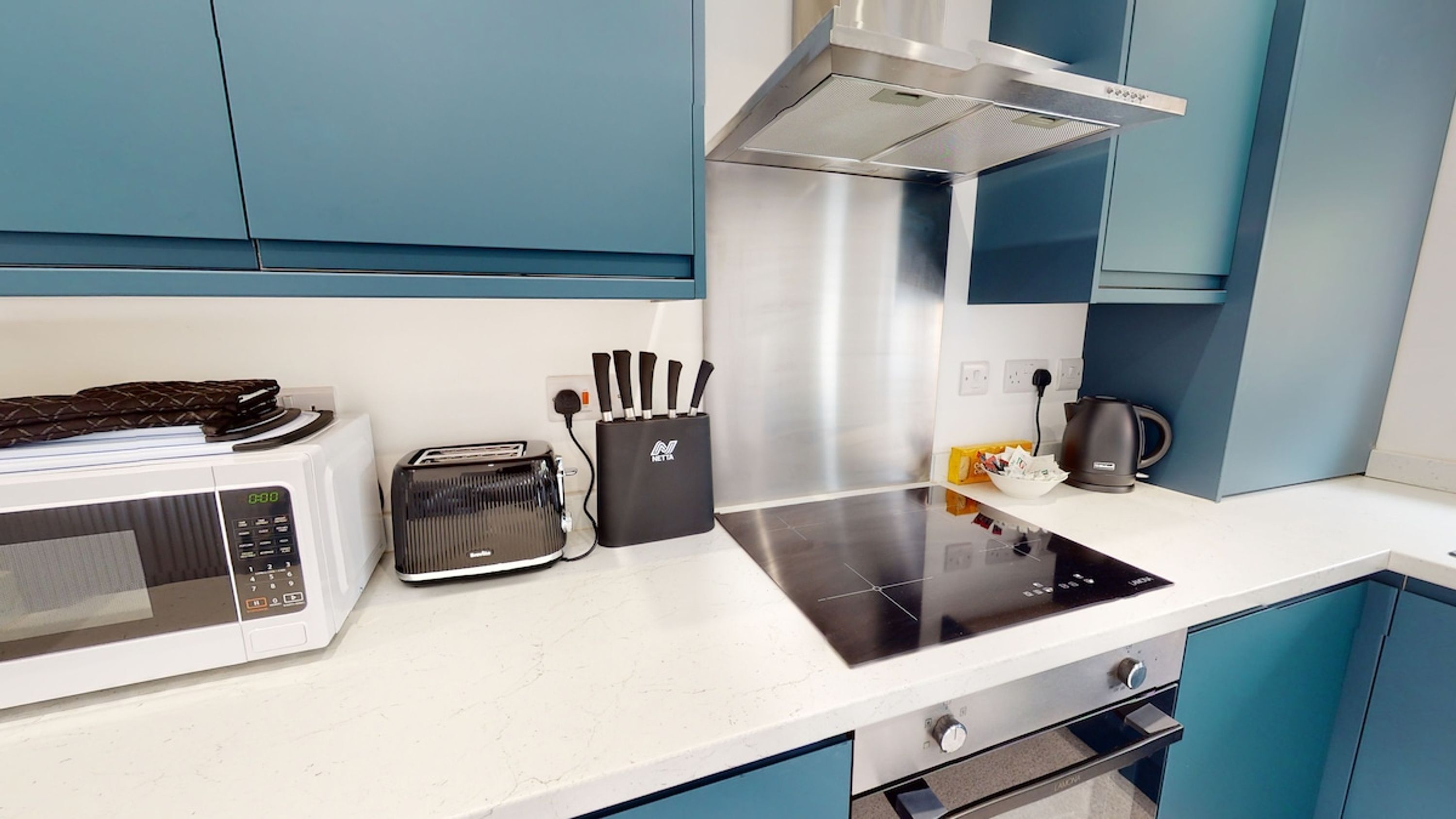 A modern kitchen with a microwave, toaster, knife block, kettle, and a stovetop.