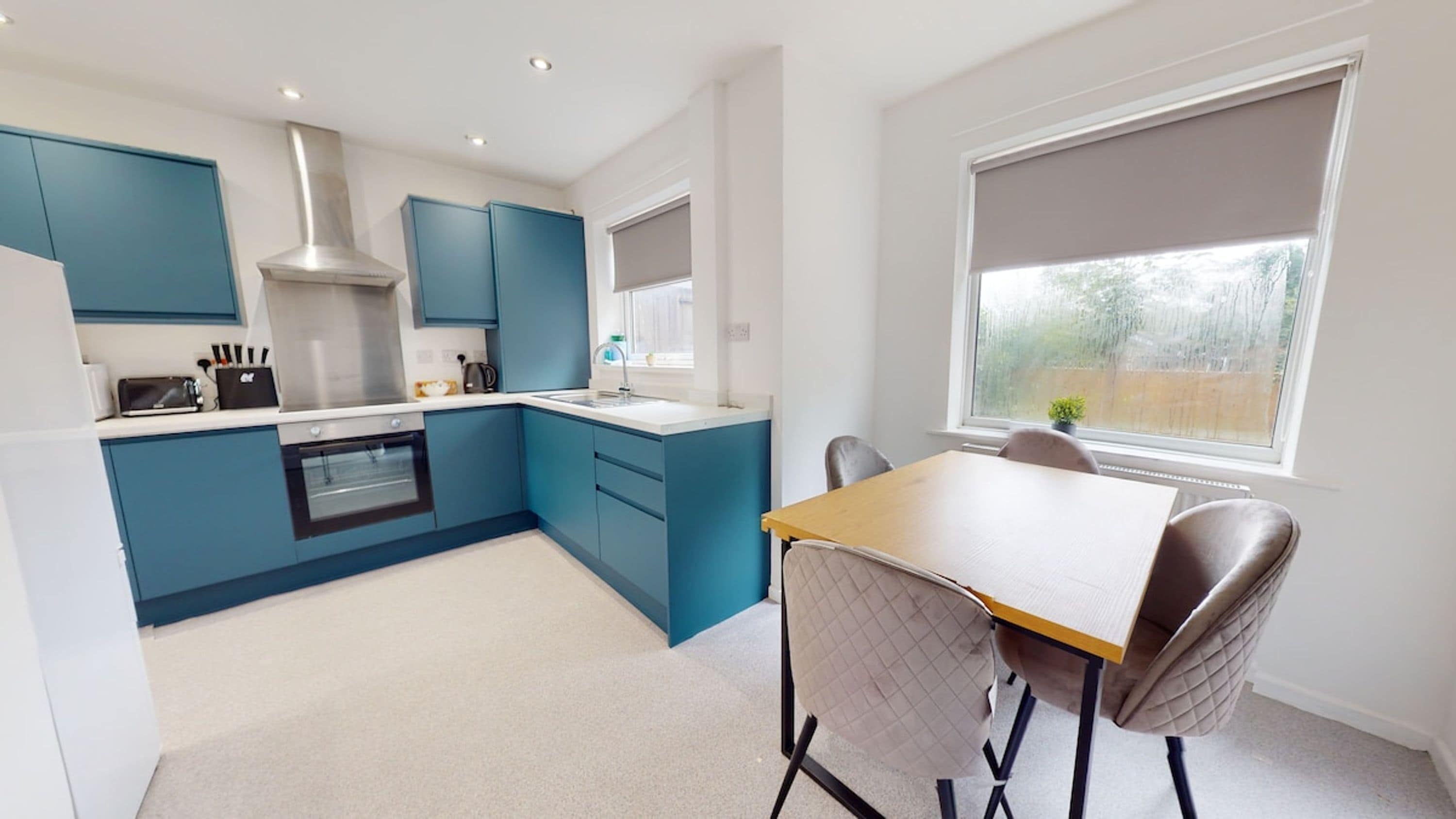 A modern kitchen with blue cabinets, a built-in oven, and a dining area with a table and chairs.