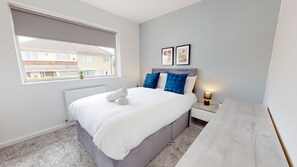A bedroom with a bed, a nightstand, a lamp, and a window. - Daventry House Horizon Stays (Stockton-on-Tees)