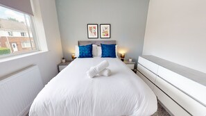 Ein Hotelzimmer mit einem großen Bett, zwei Nachttischen, einem Fenster und zwei gerahmten Bildern an der Wand.