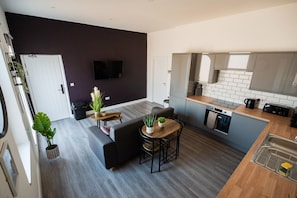 Eine moderne Küche mit eingebautem Backofen, ein Essbereich mit einer Couch und einem kleinen Tisch sowie ein an der Wand montierter Fernseher.