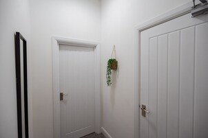 Un pasillo con dos puertas blancas, una con marco negro, y una planta colgante.
