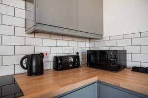 Una cocina moderna con paredes de azulejos blancos, encimera de madera, hervidor, tostadora y microondas.