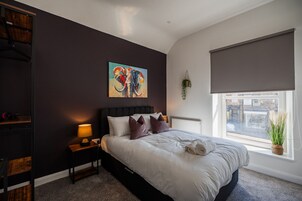 Un dormitorio con una cama grande, una mesita de noche con lámpara, un cuadro en la pared y una ventana con vistas.