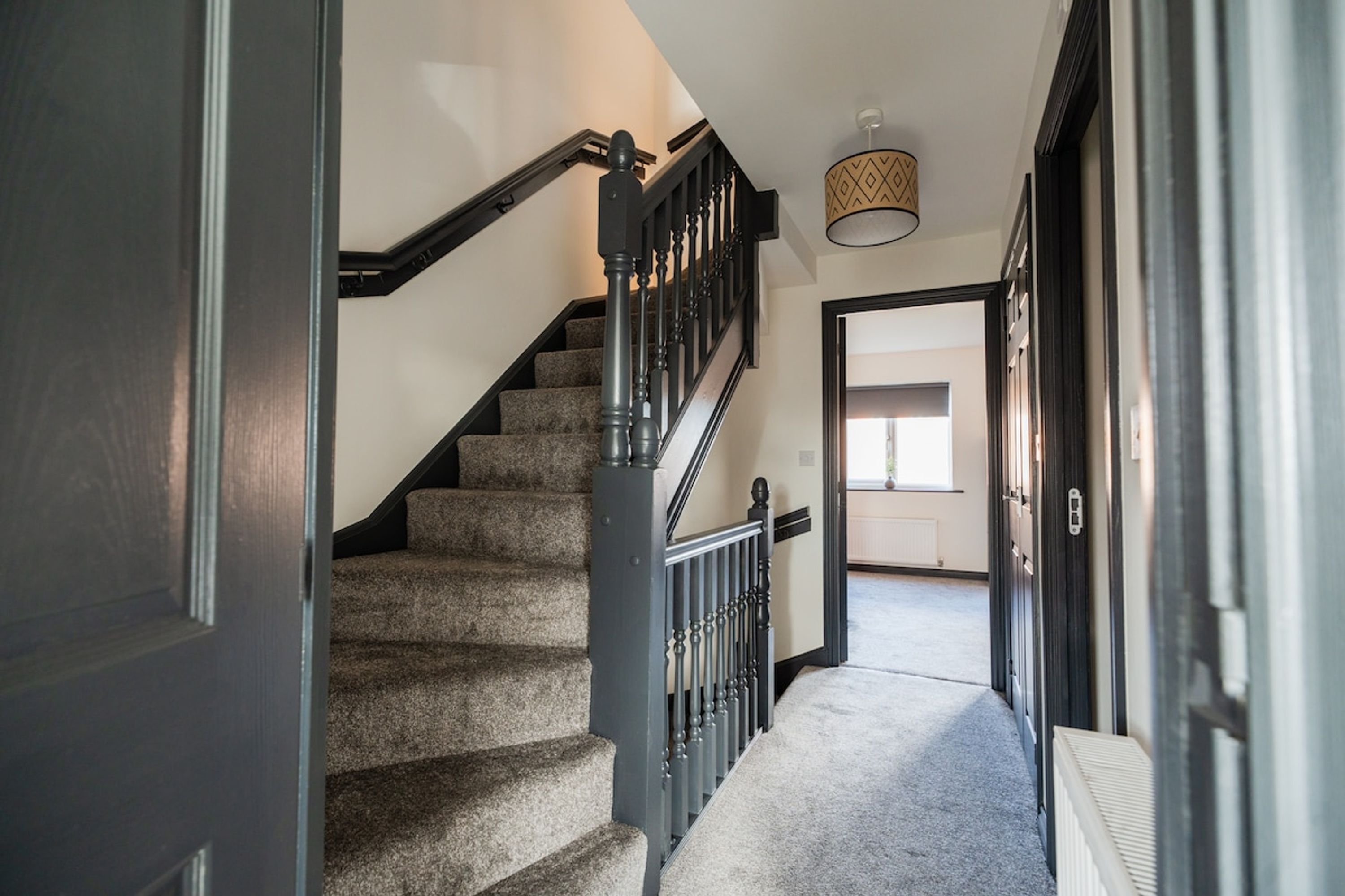A staircase with carpeted steps and a black railing, leading to an open doorway.