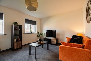 A living room with a sofa, a TV, a coffee table, a bookshelf, and a window with blinds. - Nightingale House Horizonstays (Stockton-on-Tees)