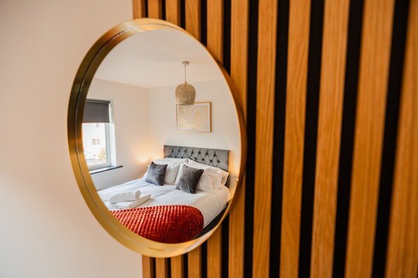 Una camera da letto con un letto, una finestra, uno specchio fissato al muro e un lampadario.