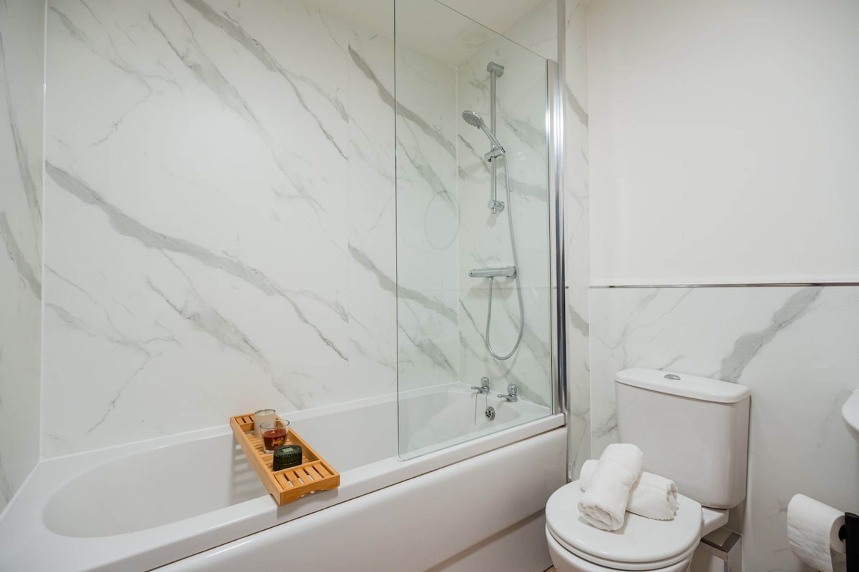 Et badeværelse med en brusekabine i glas, et hvidt toilet og en træbakke med toiletartikler.