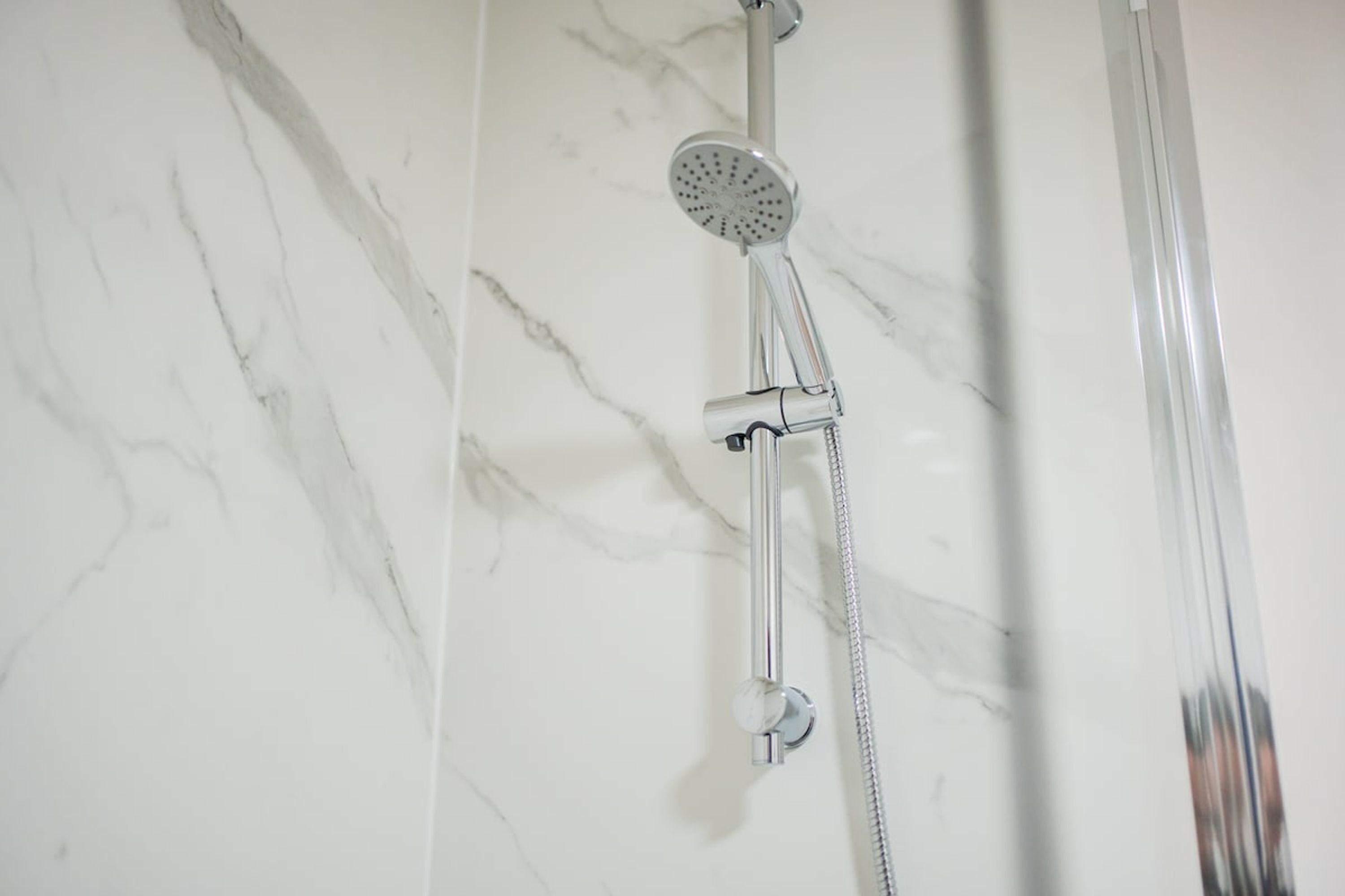 Une douche équipée d’un pommeau de douche à main et d’un robinet fixé au mur.