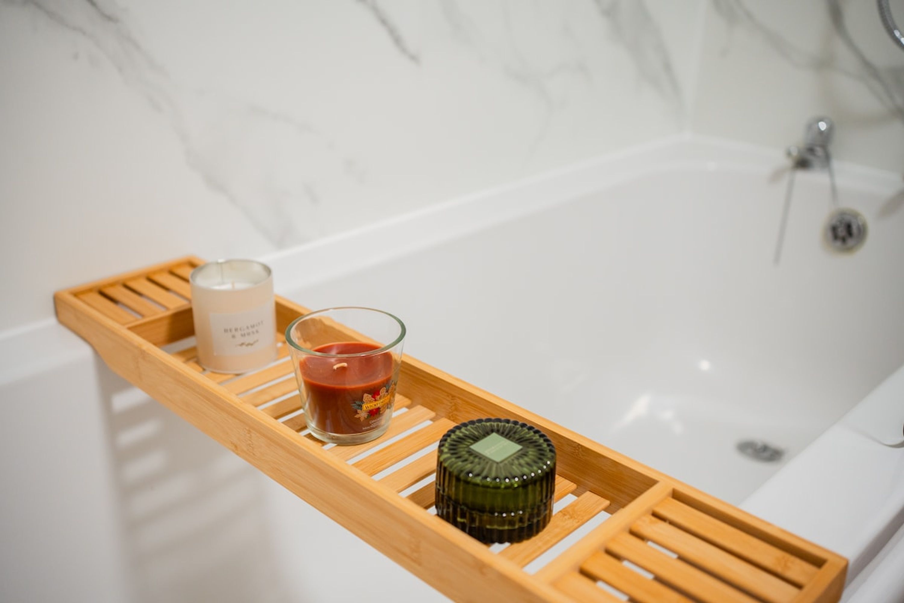A wooden tray with a candle, a glass candle holder, and a bottle on a bathroom counter.