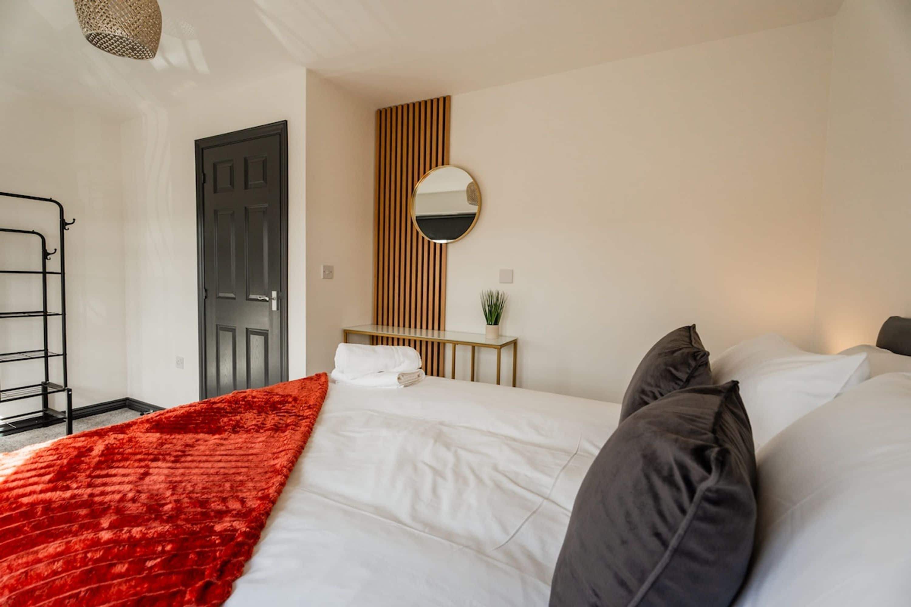 Habitación de hotel con una cama, una mesita de noche, un espejo, una puerta y un estante fijado a la pared.