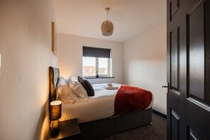 Ein Schlafzimmer mit Bett, Nachttischlampe, Fenster und Tür.