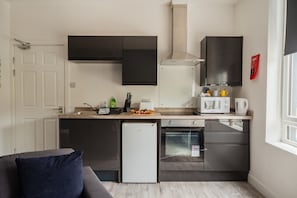 Eine kleine Küche mit Kühlschrank, Mikrowelle und Backofen, einem Spülbecken und einem Fenster für natürliches Licht.