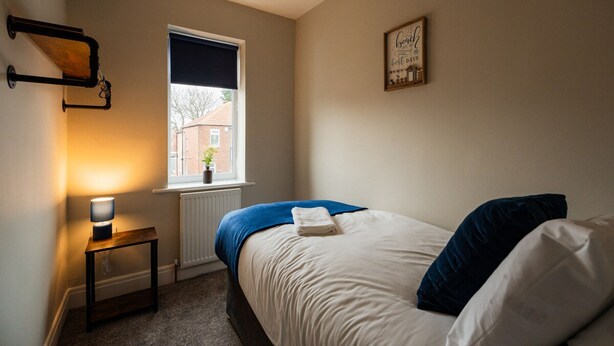 A bedroom with a bed, a bedside table, a lamp, a window, and a radiator. - 3 bed Contractor Accommodation Redcar (Redcar)