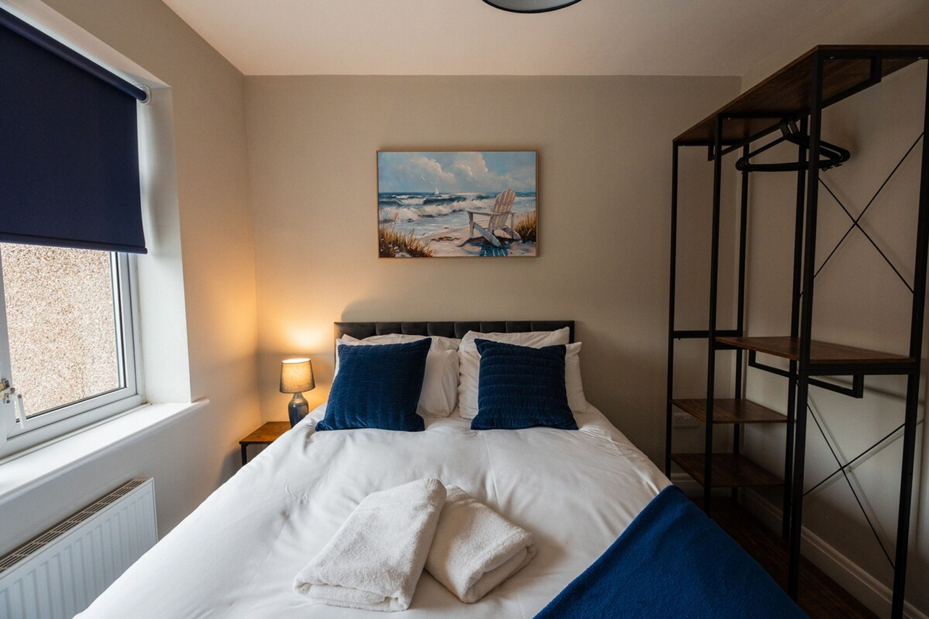 Une chambre à coucher avec un lit, un tableau, une fenêtre et une étagère en métal.
