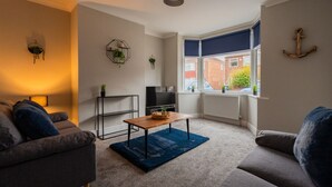 A living room with a sofa, a coffee table, a TV, and a window with a view of a brick building. - 3 bed Contractor Accommodation Redcar (Redcar)