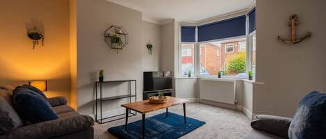 A living room with a sofa, a coffee table, a TV, and a window with a view of a brick building.