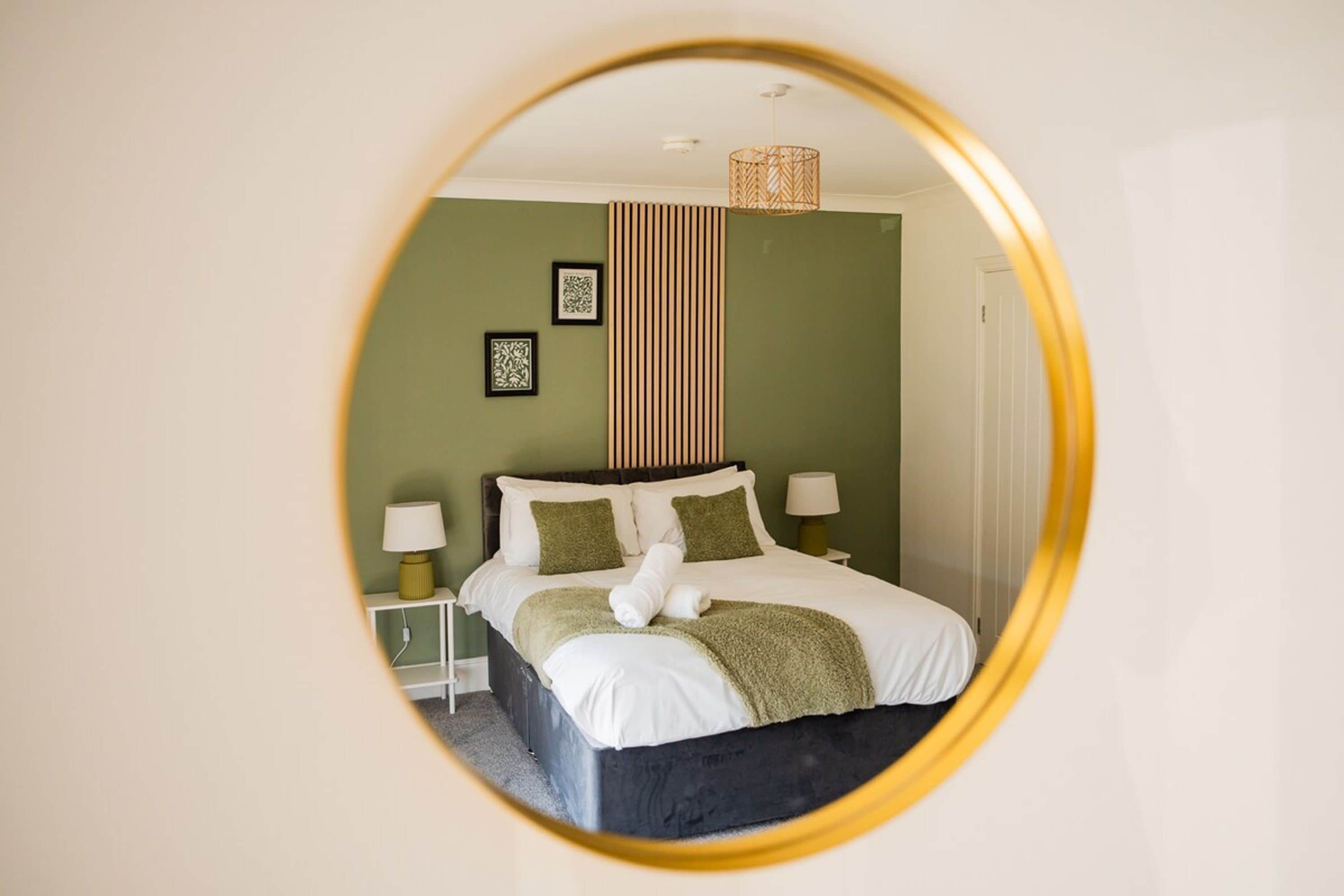 A circular mirror reflecting a bedroom with a bed, two bedside tables, and a hanging light fixture.