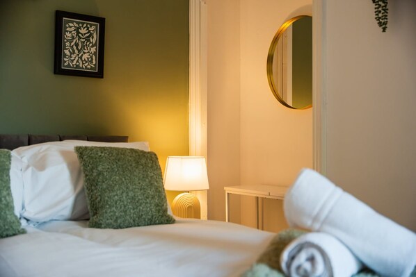 A hotel room with a bed, pillows, a bedside table with a lamp, and a wall-mounted mirror. - Rockliffe House Horizon Stays (Middlesbrough)