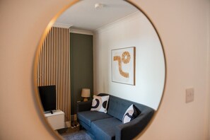 A room with a round mirror reflecting a corner with a sofa, a lamp, and a framed artwork. - Rockliffe House Horizon Stays (Middlesbrough)