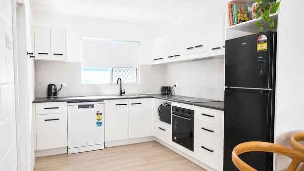 A modern kitchen with white cabinetry, a black refrigerator, and a wooden chair. - Convenient Townsville Stay Near Hospital and CBD (Pimlico)