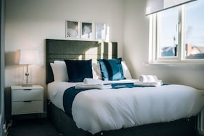 A hotel room with a bed, a nightstand, a lamp, and a window. - Freda House Horizon Stays (Sunderland)