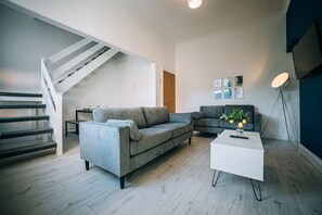 Ein modernes Wohnzimmer mit einem grauen Sofa, einem weißen Couchtisch und einer Treppe.