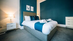 A hotel room with a large bed, a bedside table with a lamp, a dresser, and two framed pictures on the wall. - Freda House Horizon Stays (Sunderland)