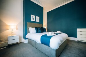 A hotel room with a large bed, a bedside table with a lamp, a dresser, and two framed pictures on the wall. - Freda House Horizon Stays (Sunderland)