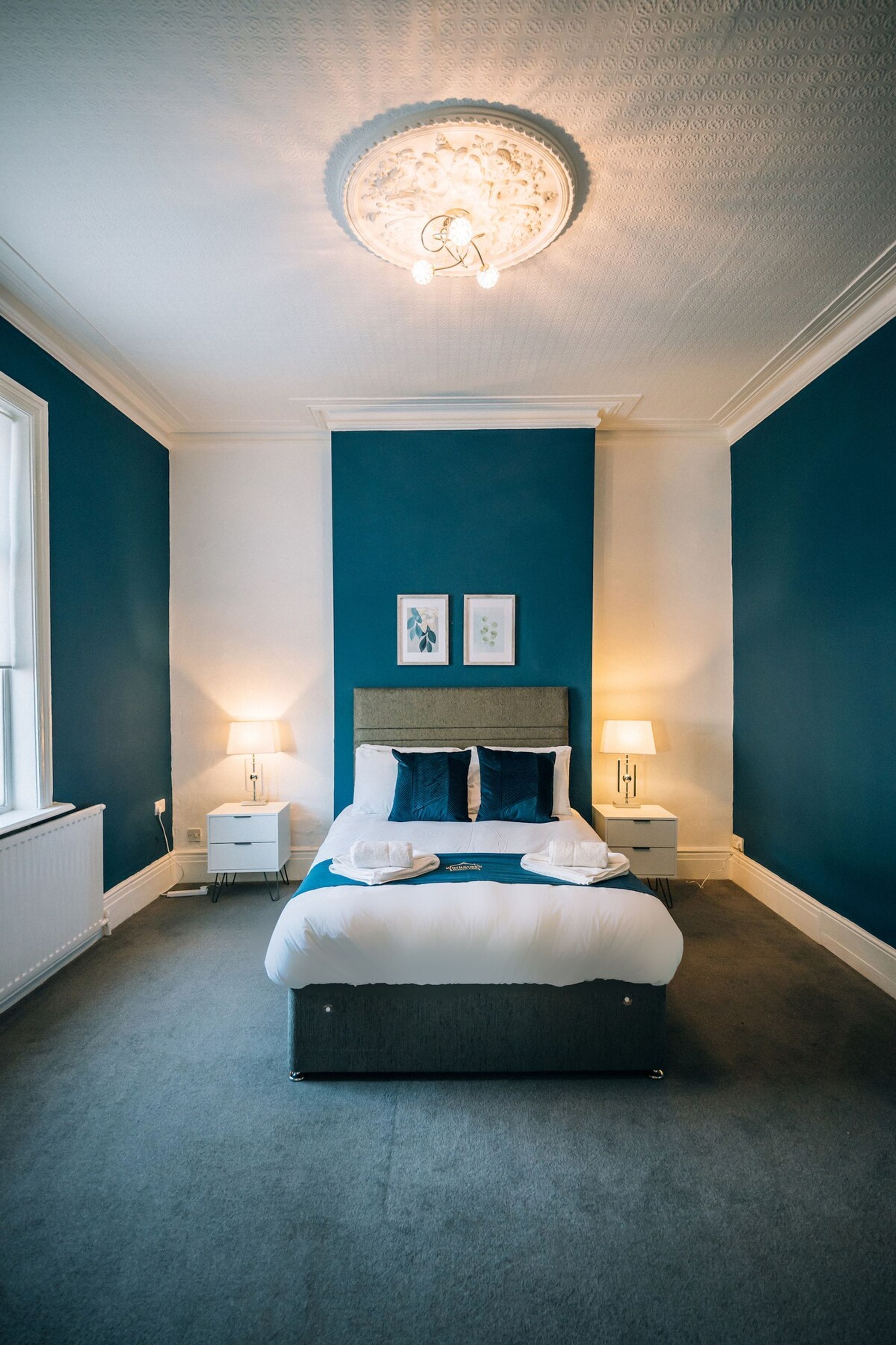 Een slaapkamer met een groot bed, twee nachtkastjes, een plafondlamp en twee aan de muur hangende foto's.