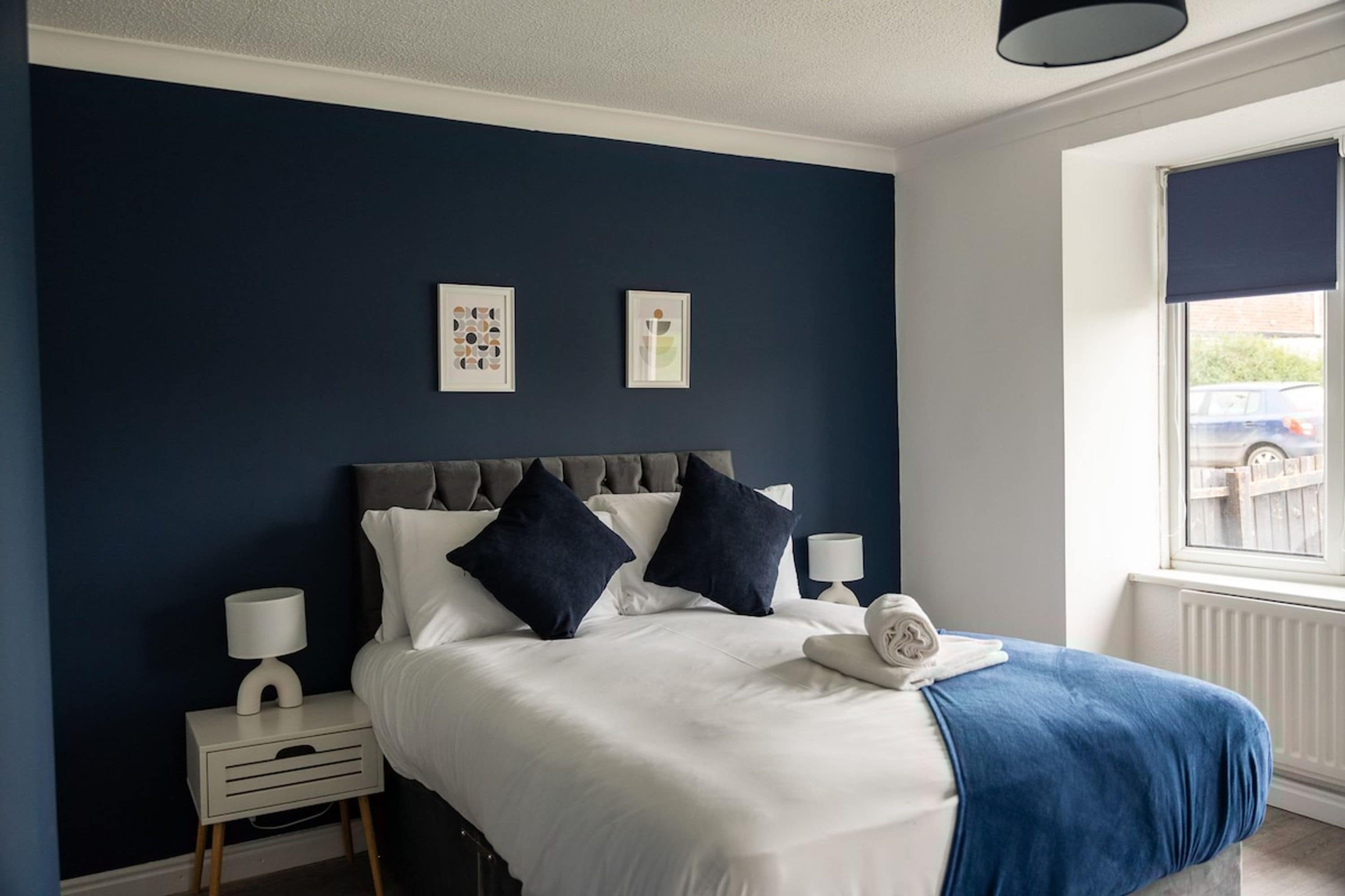A bedroom with a bed, two bedside tables, a window, and artwork on the wall.