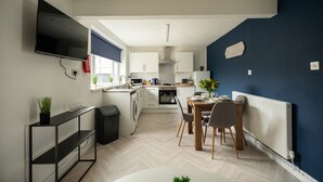 A modern kitchen with white cabinets, a dining area with a wooden table and chairs, and a blue accent wall. - Renvyle House Horizon Stays (Stockton-on-Tees)