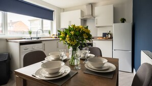 A modern kitchen with white cabinets, a dining table set with bowls and glasses, and a vase with yellow flowers. - Renvyle House Horizon Stays (Stockton-on-Tees)