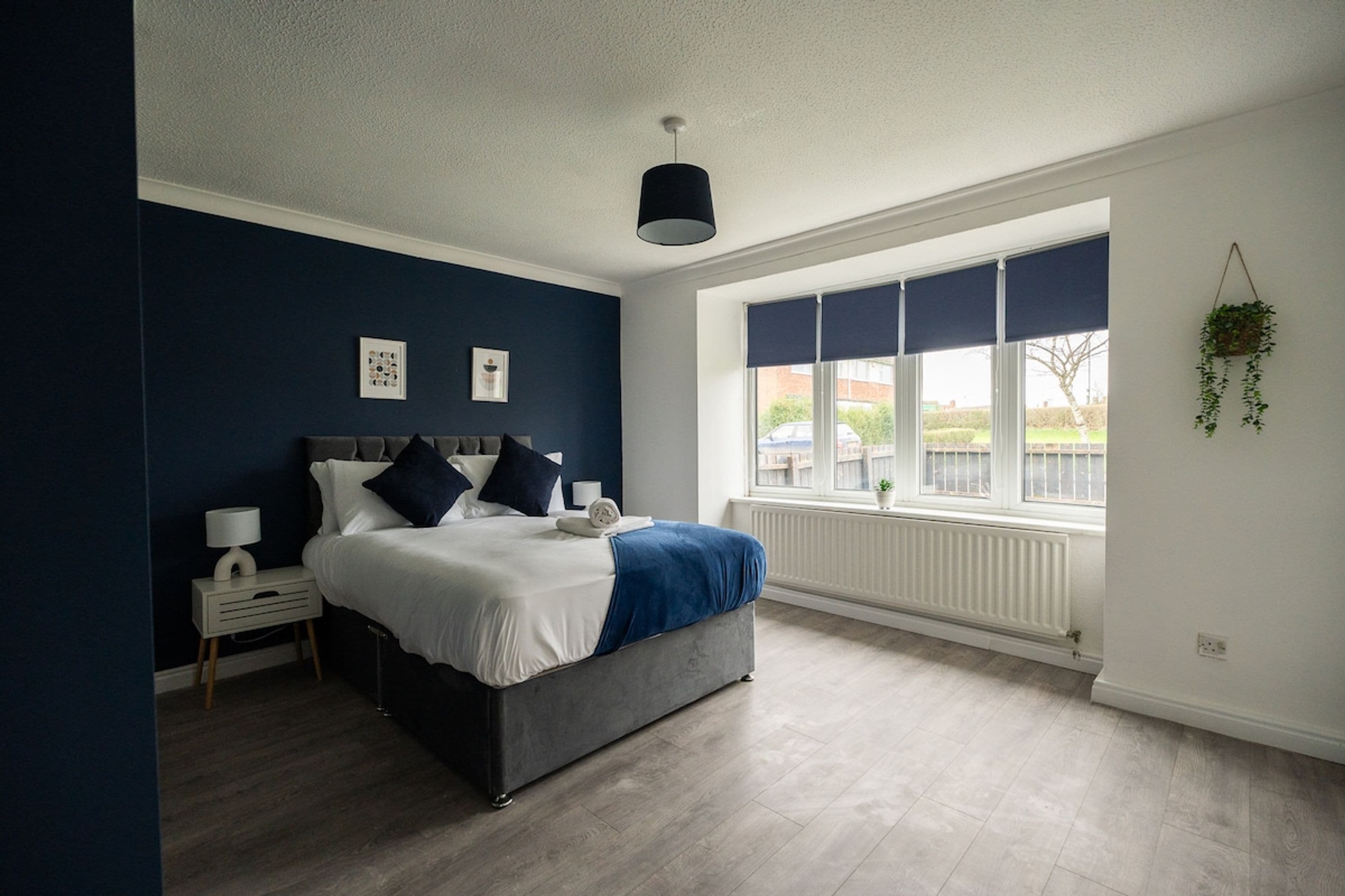 A bedroom with a bed, bedside table, lamp, and a window with blinds.