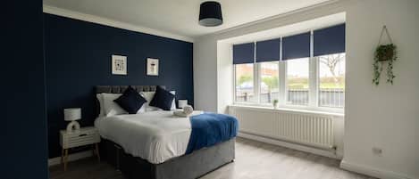 A bedroom with a bed, bedside table, lamp, and a window with blinds.