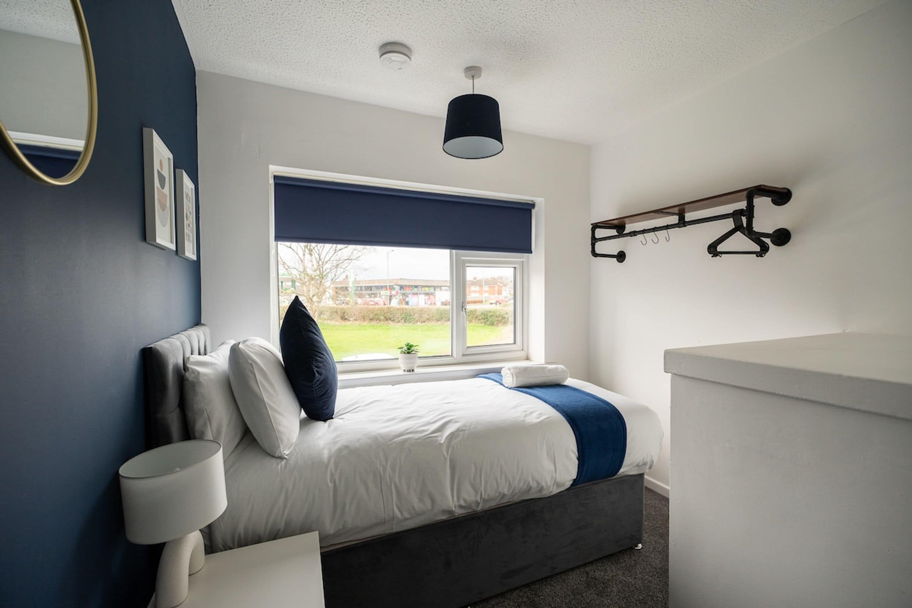 A bedroom with a bed, bedside lamps, a window with a view, a ceiling light, and a coat rack.