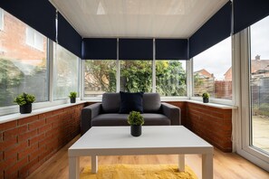 A sunroom with a grey sofa, a white table, and potted plants. - Renvyle House Horizon Stays (Stockton-on-Tees)