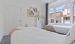 A hotel room with two beds, a radiator, a window with a view of buildings, and a door. - Lord House by Horizon Stays (Redcar)