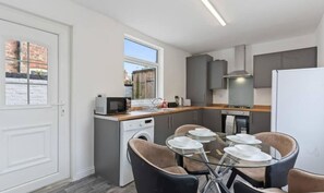 A modern kitchen with a dining area, including a table set for four, a microwave, and a dishwasher. - Lord House by Horizon Stays (Redcar)