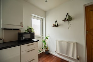 A kitchen with a microwave, a window, a radiator, and a door. - Jubilee House Horizon Stays (Middlesbrough)