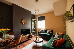 A modern living room with a dark accent wall, a green sofa, a TV, a dining area with chairs, and a coffee table. - Jubilee House Horizon Stays (Middlesbrough)