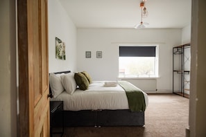 A bedroom with a bed, a radiator, a window with a blind, and a hanging light fixture. - Jubilee House Horizon Stays (Middlesbrough)