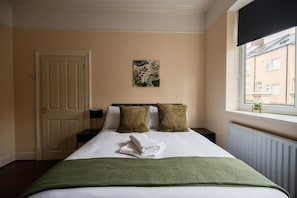 A hotel room with a bed, a window, a door, and a painting on the wall. - Jubilee House Horizon Stays (Middlesbrough)