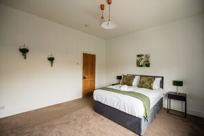 A bedroom with a bed, bedside tables, a door, and a hanging plant. - Jubilee House Horizon Stays (Middlesbrough)