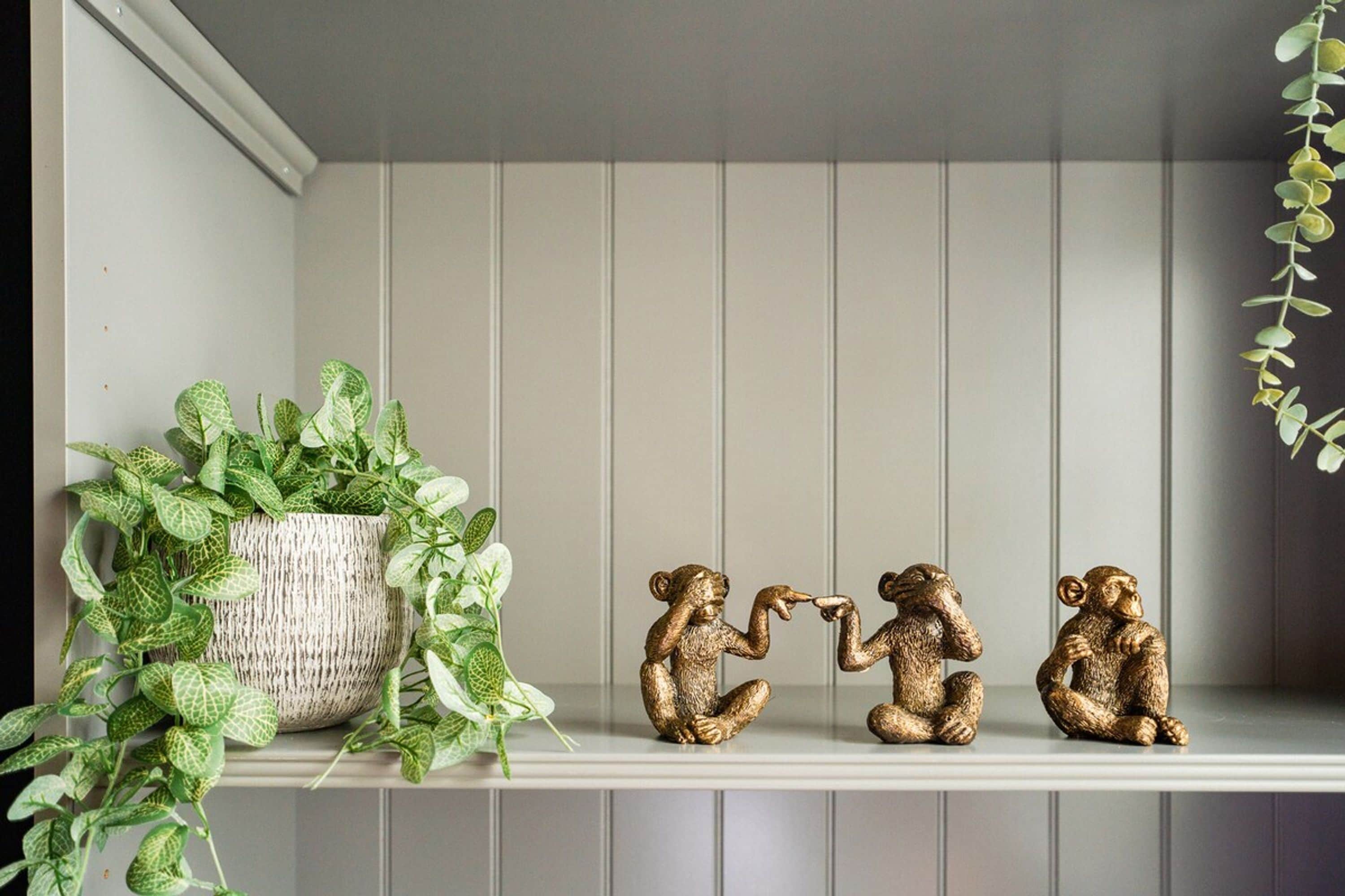 A shelf with a potted plant and three golden figurines.