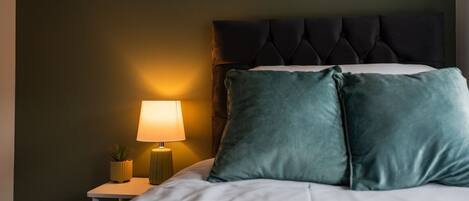 A neatly made bed with two pillows, a bedside lamp, and a small potted plant on a nightstand.